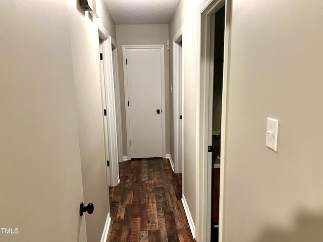 hallway with dark wood-type flooring, baseboards, and a textured ceiling