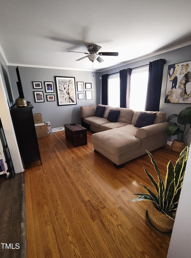 living area featuring baseboards, crown molding, a ceiling fan, and wood finished floors