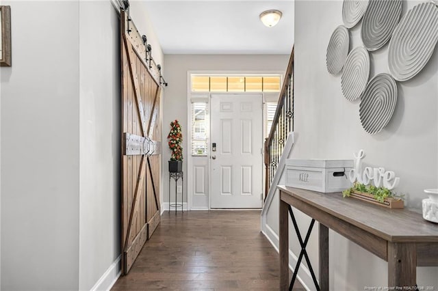 foyer featuring a barn door, dark wood-type flooring, stairway, and baseboards