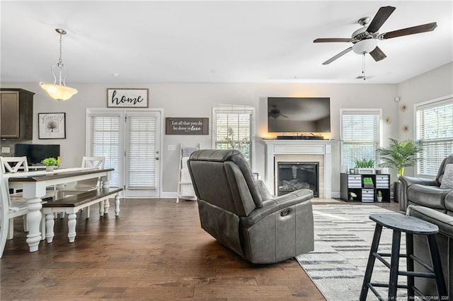 living area with a glass covered fireplace, dark wood finished floors, baseboards, and ceiling fan