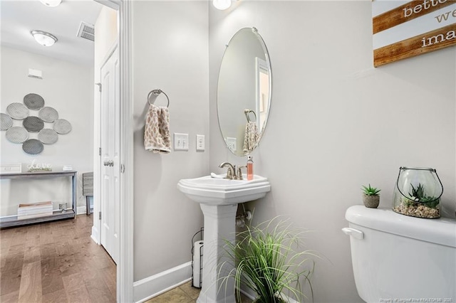 bathroom with toilet, a sink, visible vents, wood finished floors, and baseboards