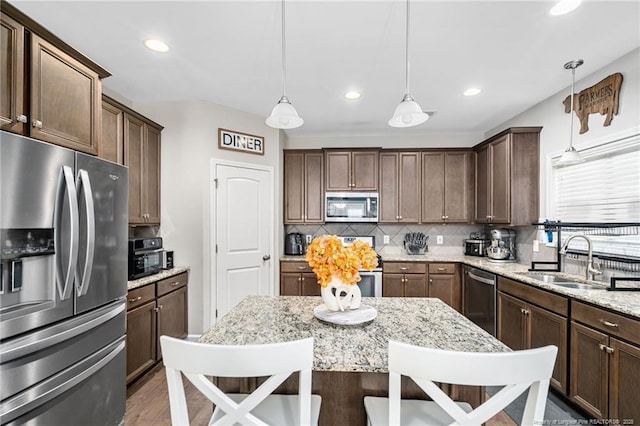 kitchen featuring a breakfast bar, decorative light fixtures, decorative backsplash, appliances with stainless steel finishes, and a sink