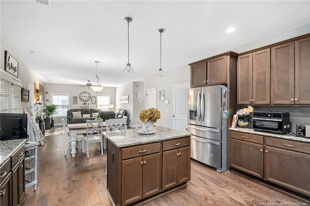 kitchen with dark wood-style floors, stainless steel refrigerator with ice dispenser, decorative light fixtures, and open floor plan