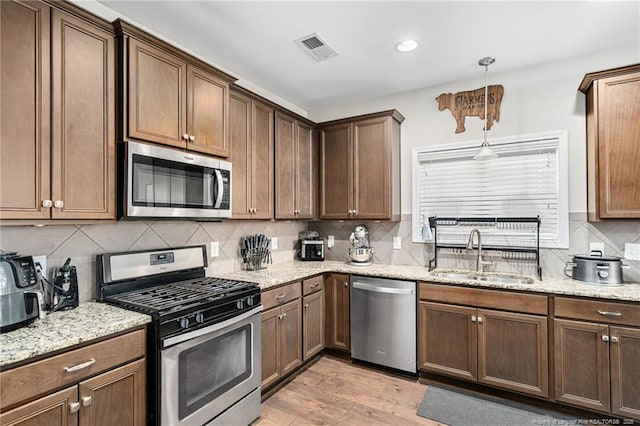 kitchen with light stone counters, stainless steel appliances, visible vents, light wood-style flooring, and a sink