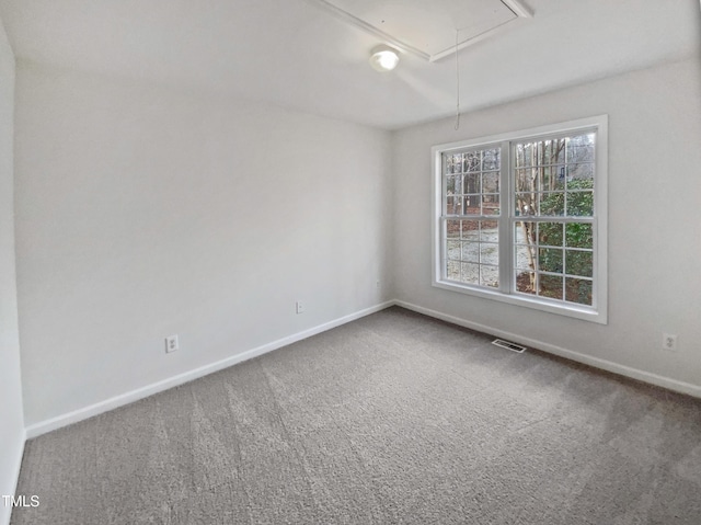 carpeted empty room with attic access, visible vents, and baseboards