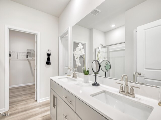 full bathroom featuring wood finished floors, visible vents, a sink, a shower stall, and a spacious closet