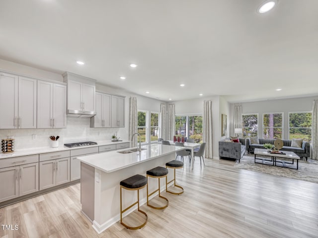 kitchen with a breakfast bar area, stainless steel gas cooktop, a kitchen island with sink, a sink, and open floor plan