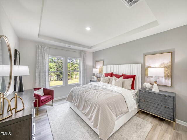 bedroom featuring a tray ceiling, light wood-style floors, and visible vents