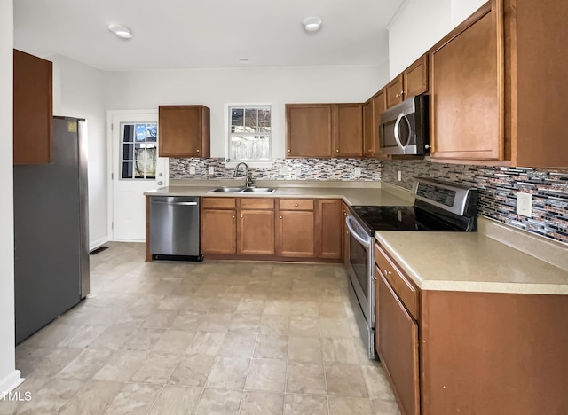 kitchen with appliances with stainless steel finishes, decorative backsplash, a sink, and brown cabinets