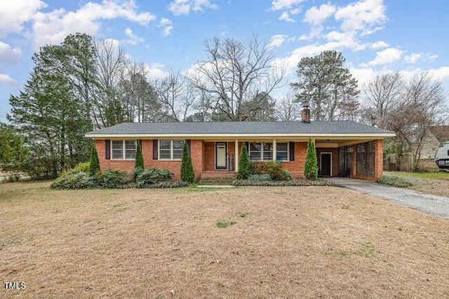 ranch-style home featuring brick siding, a chimney, an attached carport, driveway, and a front lawn