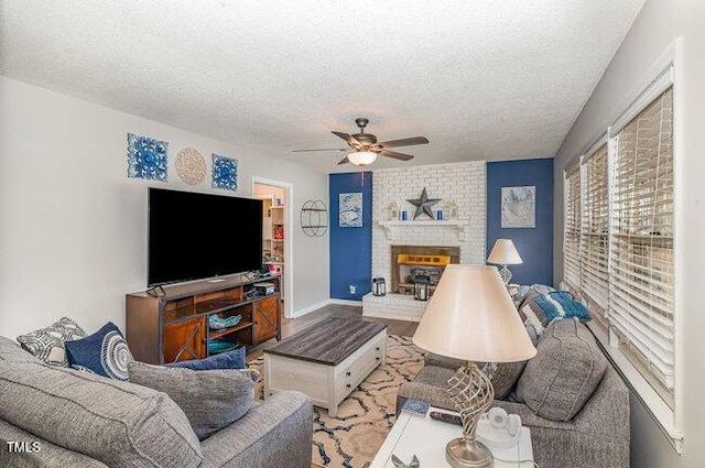 living area featuring a fireplace, a textured ceiling, baseboards, and ceiling fan