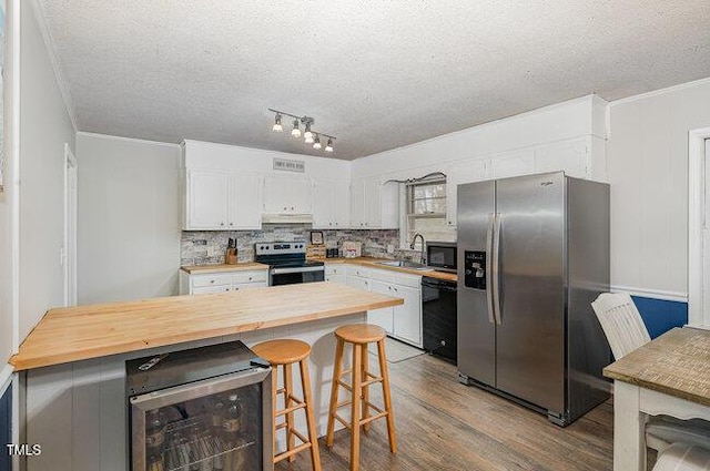 kitchen with beverage cooler, under cabinet range hood, black appliances, wooden counters, and a sink