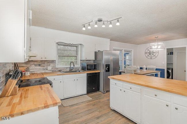 kitchen with stainless steel appliances, butcher block counters, a sink, white cabinetry, and washer / dryer