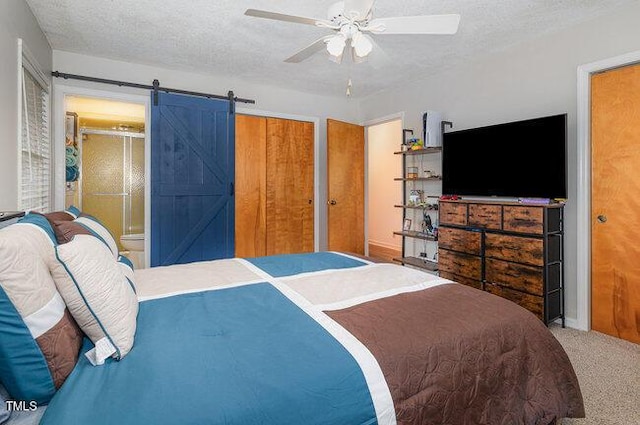 carpeted bedroom featuring a barn door, connected bathroom, ceiling fan, and a textured ceiling