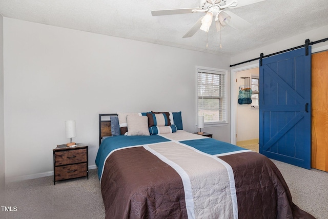 bedroom featuring a textured ceiling, carpet floors, a barn door, and a ceiling fan