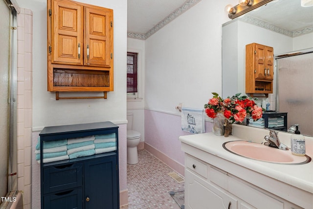 bathroom featuring toilet, a shower with door, baseboards, and vanity