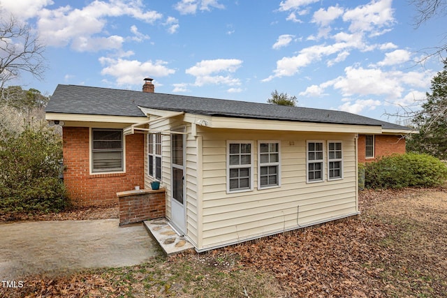 exterior space featuring brick siding, a chimney, a patio area, and a shingled roof