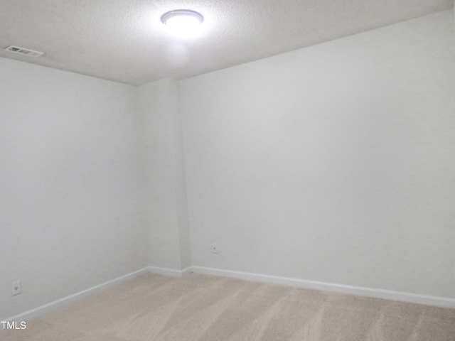 spare room with a textured ceiling, baseboards, visible vents, and light carpet