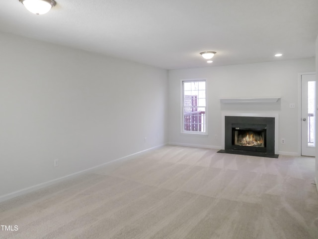 unfurnished living room with recessed lighting, baseboards, a fireplace with flush hearth, and light carpet