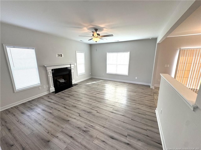 unfurnished living room with a ceiling fan, a fireplace with flush hearth, baseboards, and wood finished floors