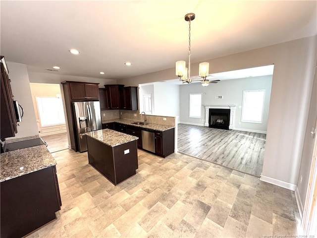 kitchen featuring a sink, a center island, dark brown cabinets, appliances with stainless steel finishes, and light stone countertops