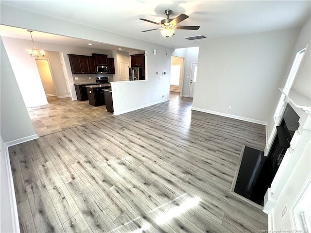 unfurnished living room featuring ceiling fan with notable chandelier, baseboards, visible vents, and light wood-style floors