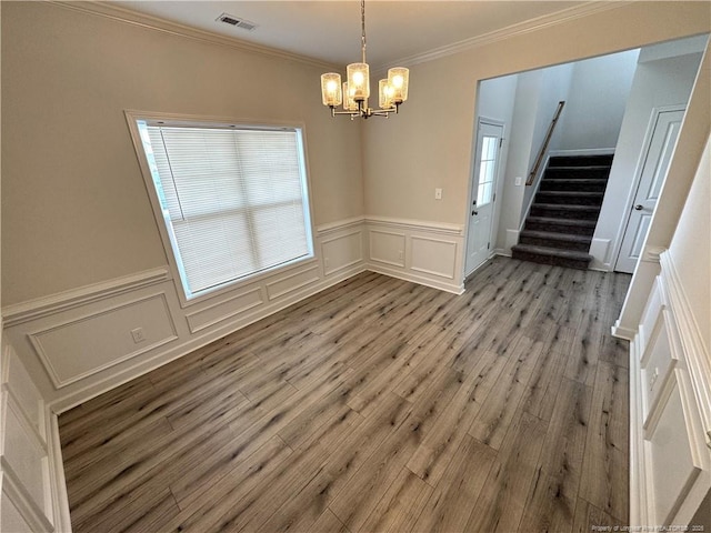 unfurnished dining area featuring crown molding, visible vents, a decorative wall, wood finished floors, and stairs