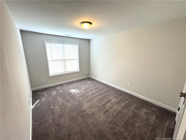 spare room featuring dark carpet and baseboards