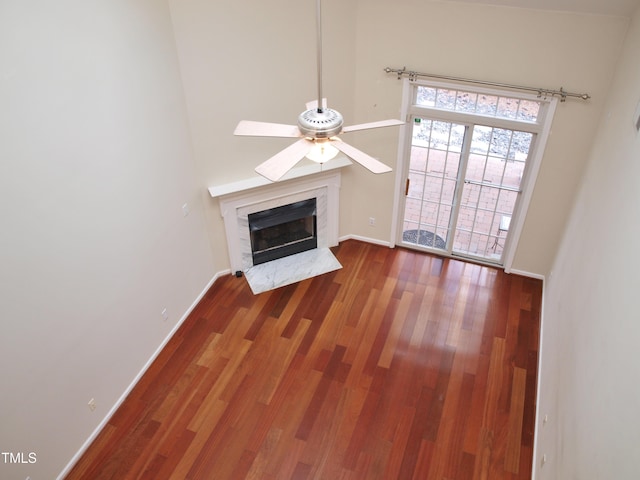 unfurnished living room with a premium fireplace, baseboards, wood finished floors, and a ceiling fan