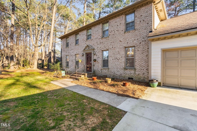 colonial house with driveway, crawl space, an attached garage, a front lawn, and brick siding