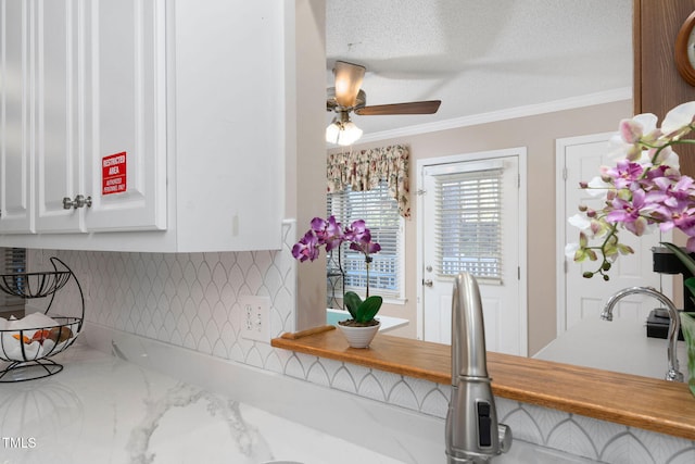 room details featuring a textured ceiling, ornamental molding, white cabinetry, and a ceiling fan