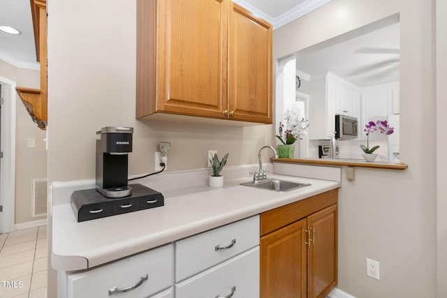 kitchen with a sink, visible vents, light countertops, ornamental molding, and stainless steel microwave