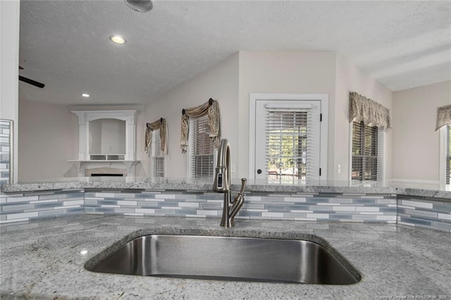 4305 Sanderosa Rd, Fayetteville, NC 28312 - kitchen with decorative backsplash, a textured ceiling, stone counters, a fireplace, and a sink