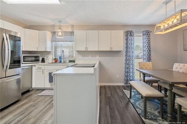 kitchen with stainless steel appliances, light countertops, white cabinetry, a sink, and wood finished floors