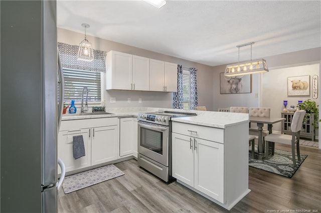 kitchen featuring a peninsula, a sink, white cabinets, appliances with stainless steel finishes, and light wood finished floors