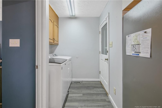 clothes washing area featuring a textured ceiling, washing machine and dryer, wood finished floors, baseboards, and cabinet space