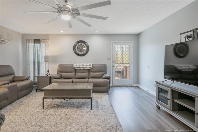 living room with ceiling fan, a textured ceiling, baseboards, and wood finished floors