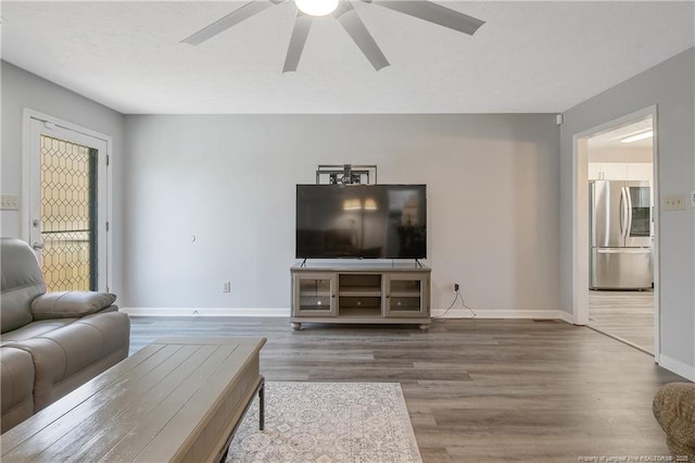 living room featuring a ceiling fan, baseboards, and wood finished floors