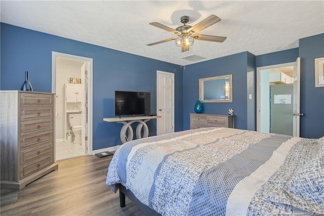 bedroom featuring a textured ceiling, connected bathroom, wood finished floors, visible vents, and a ceiling fan