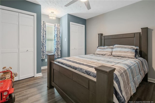 bedroom featuring a textured ceiling, baseboards, wood finished floors, and multiple closets