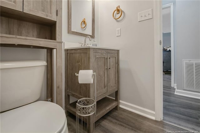 bathroom with toilet, baseboards, visible vents, and wood finished floors