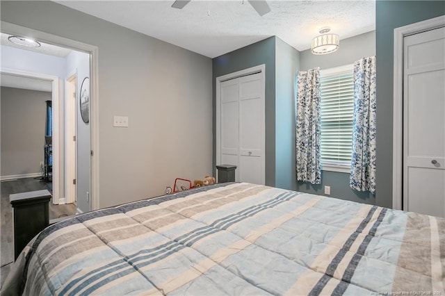 bedroom with two closets, a ceiling fan, a textured ceiling, wood finished floors, and baseboards