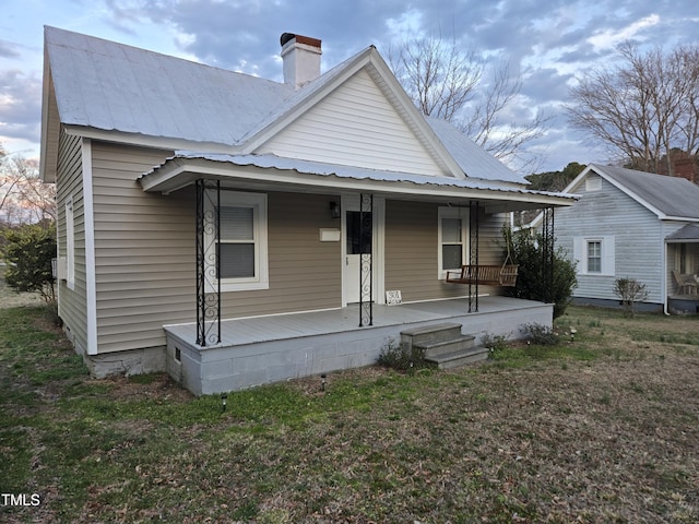 view of front of property featuring covered porch, a chimney, a front lawn, and metal roof