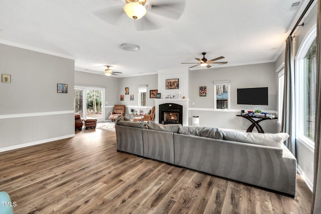 living room with a large fireplace, crown molding, baseboards, and wood finished floors