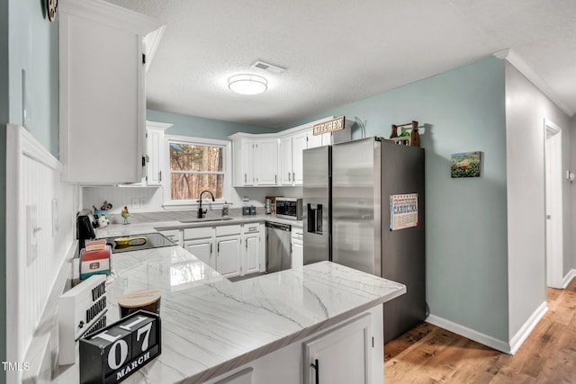 kitchen featuring stainless steel appliances, visible vents, white cabinetry, a sink, and light wood-type flooring