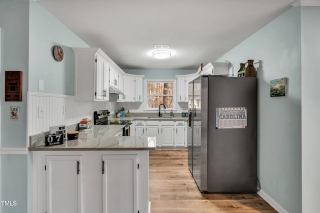 kitchen with a peninsula, a sink, light wood-style floors, white cabinets, and appliances with stainless steel finishes