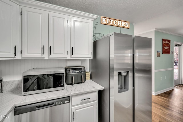 kitchen with a textured ceiling, stainless steel appliances, wood finished floors, white cabinetry, and baseboards