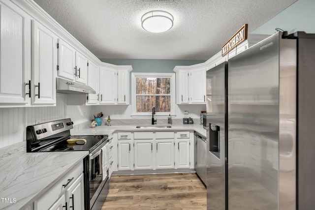 kitchen with white cabinets, light wood-style flooring, stainless steel appliances, under cabinet range hood, and a sink