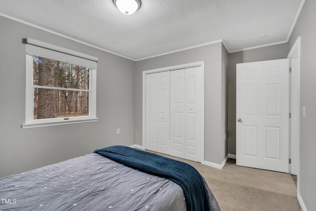 carpeted bedroom featuring a textured ceiling, baseboards, a closet, and ornamental molding