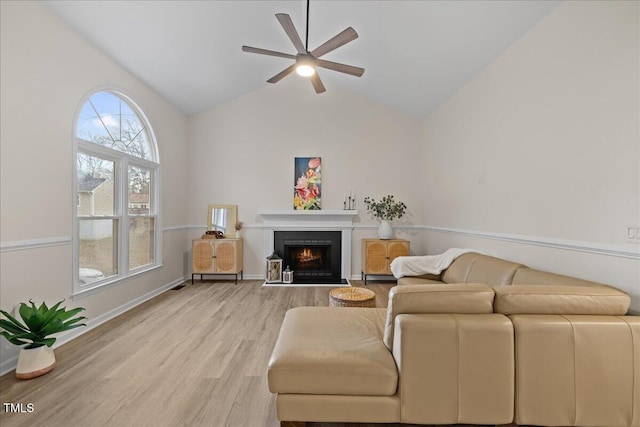 living area with light wood finished floors, lofted ceiling, a ceiling fan, a warm lit fireplace, and baseboards